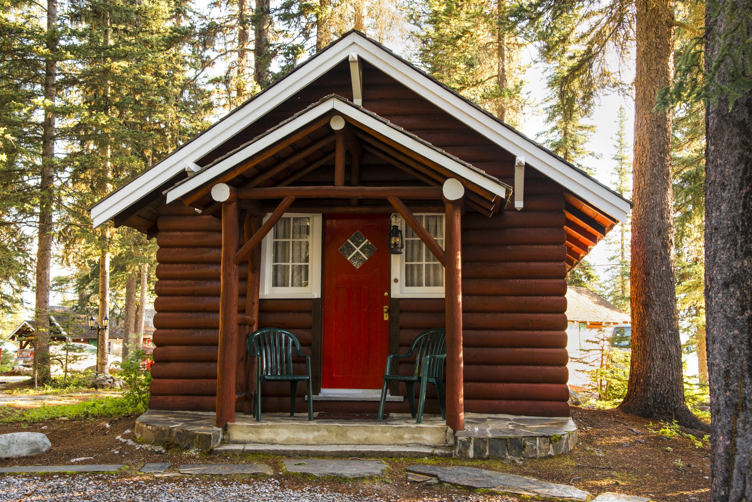 Investment Property Loans 1 A small log cabin with a red door and two green chairs on the porch, surrounded by tall trees in a forest setting.