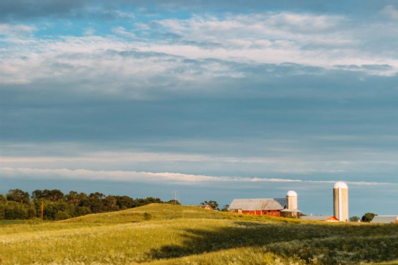 Serene rural landscape with a barn and silos under a clear blue sky.