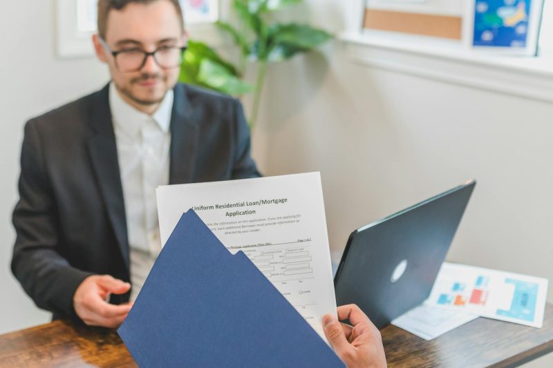 Mortgage broker and client reviewing loan documents at a table in a bright office setting.