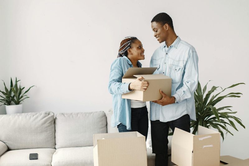 Happy young couple joyfully carrying boxes into their new home, surrounded by a welcoming entryway.
