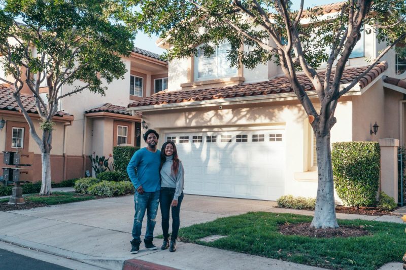 Smiling couple standing together in front of their new house, radiating happiness and pride.