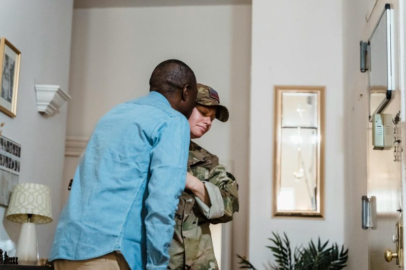 A soldier in uniform embraces their partner warmly at home, expressing love and connection.