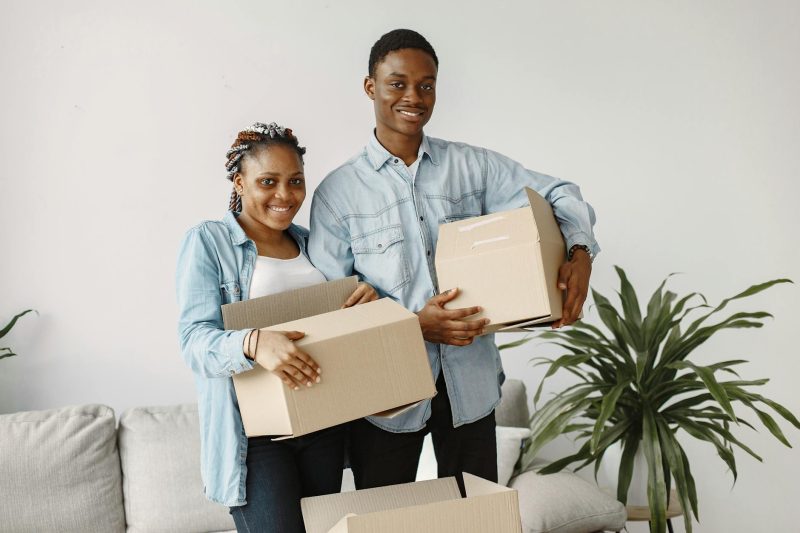 Young couple smiling while carrying cardboard boxes in their new home.