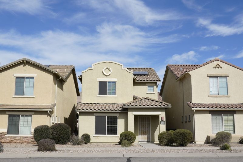 Three adjacent homes in a Tucson, Arizona suburban neighborhood under a clear blue sky.