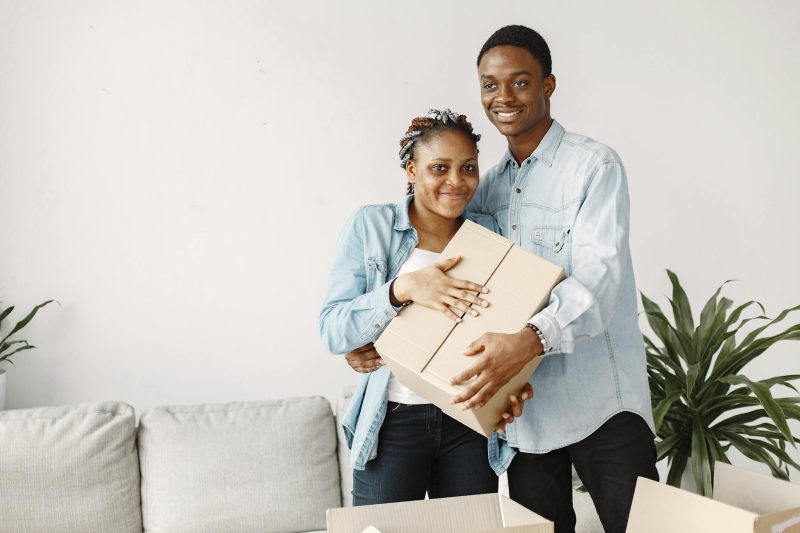 Joyful couple carrying a cardboard box in their bright new living room filled with natural light.