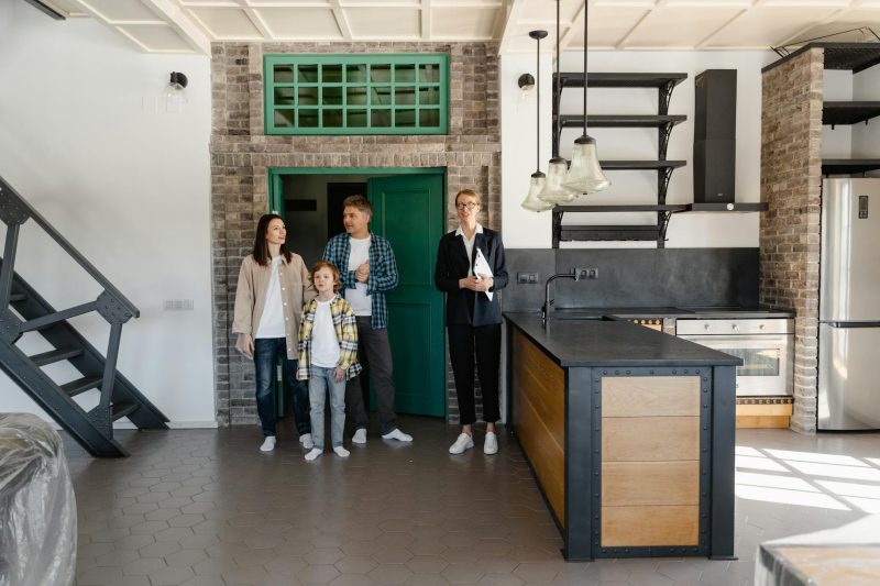 A family and a realtor explore a spacious, modern industrial-style kitchen in a new home.