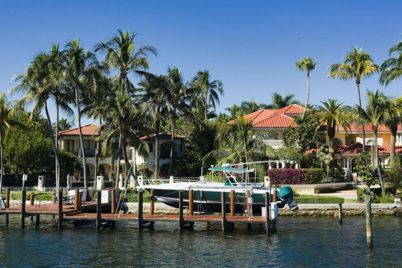 Luxury waterfront homes surrounded by palm trees and a boat docked in Fort Lauderdale, Florida.