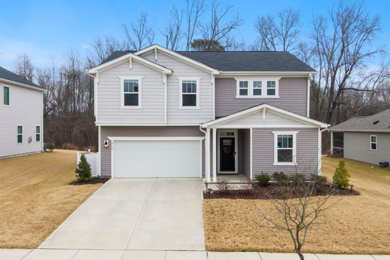 Charming two-story suburban home with a garage, surrounded by green lawn and trees in Fuquay-Varina, NC.