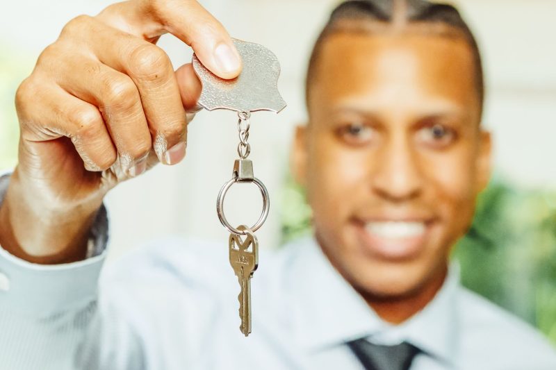 A smiling real estate agent holds a large house key, symbolizing a successful home purchase.