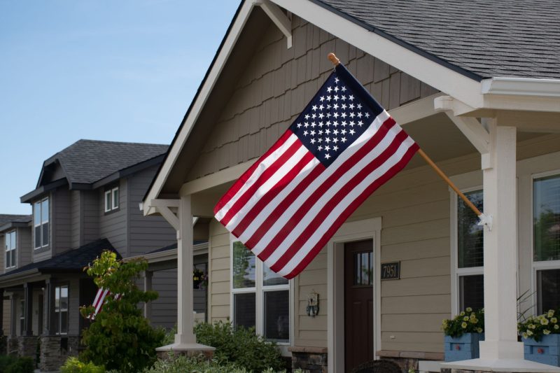 Home 9 Vibrant American flag hanging outside a stylish suburban house on a sunny day.
