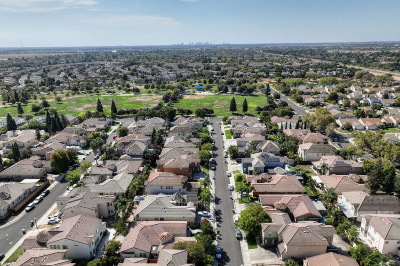 Home 10 Aerial view of a Sacramento suburb featuring rows of houses surrounded by lush greenery on a sunny day.