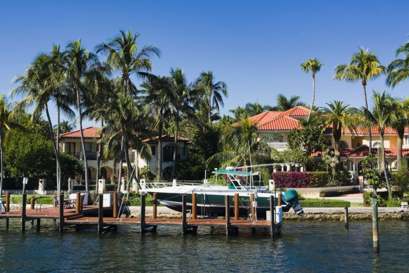 Home 16 Luxury waterfront homes with palm trees and a boat docked along the shoreline in Fort Lauderdale, Florida.
